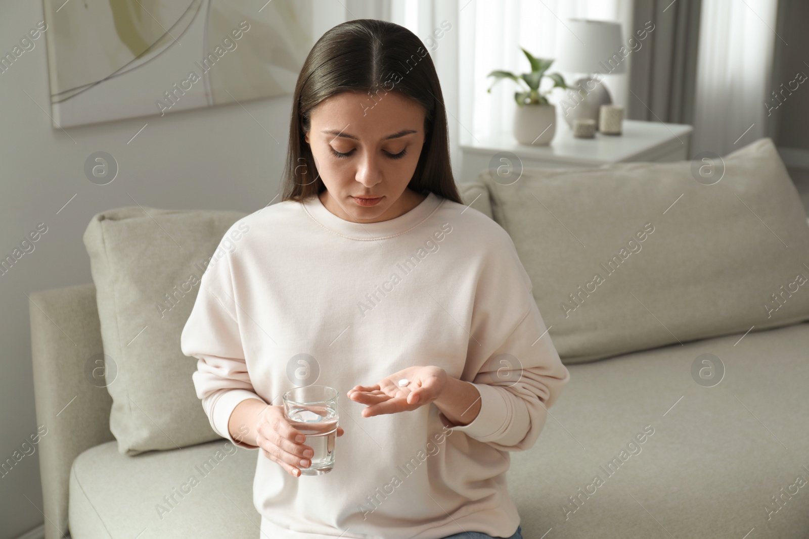 Photo of Woman with abortion pill and water on sofa indoors