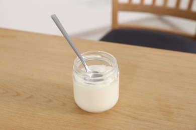 Jar of delicious yogurt with spoon on wooden table