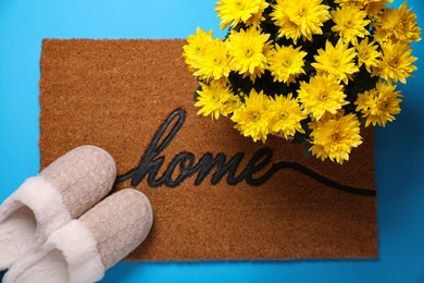 Photo of Doormat with word Home, slippers and flowers on light blue background, flat lay