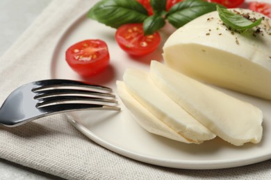 Photo of Delicious mozzarella with seasonings, tomatoes and fork on table, closeup