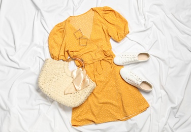 Flat lay composition with stylish yellow dress on white fabric