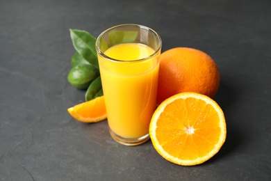 Glass of orange juice and fresh fruits on grey table