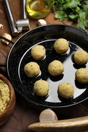 Frying pan with raw falafel balls and oil on wooden table, above view