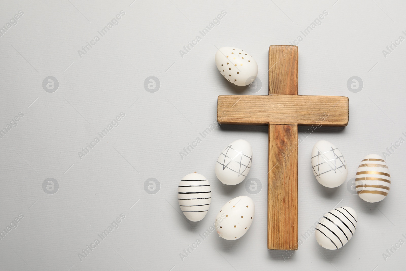 Photo of Wooden cross and painted Easter eggs on light grey background, flat lay. Space for text