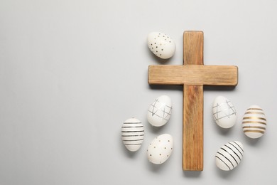 Wooden cross and painted Easter eggs on light grey background, flat lay. Space for text