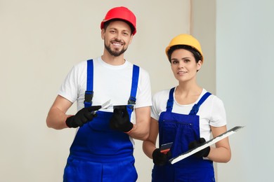 Professional workers with putty knives in hard hats near wall indoors