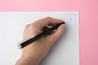 Photo of Woman erasing web drawn with erasable pen on sheet of paper against pink background, top view