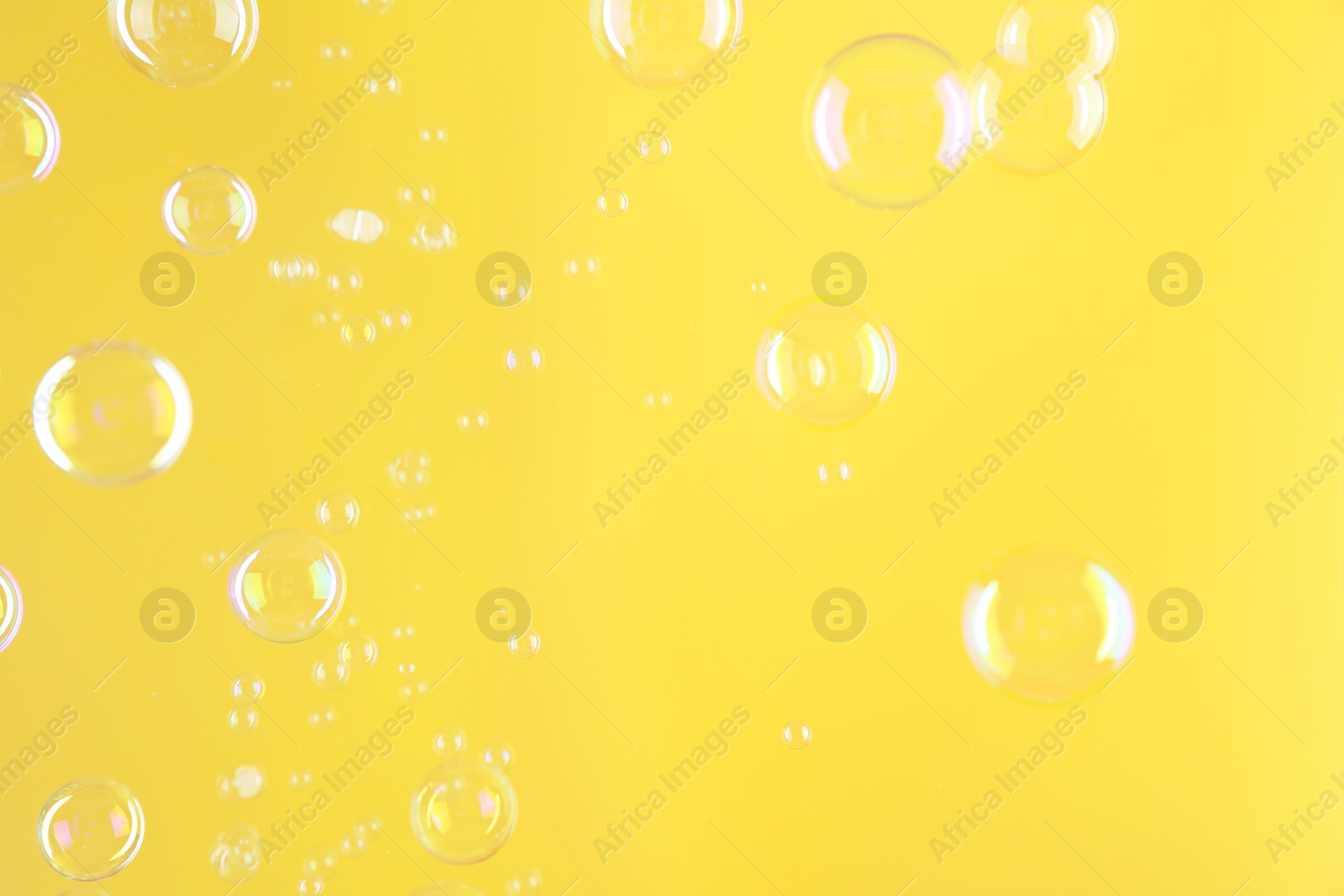 Photo of Beautiful transparent soap bubbles on yellow background