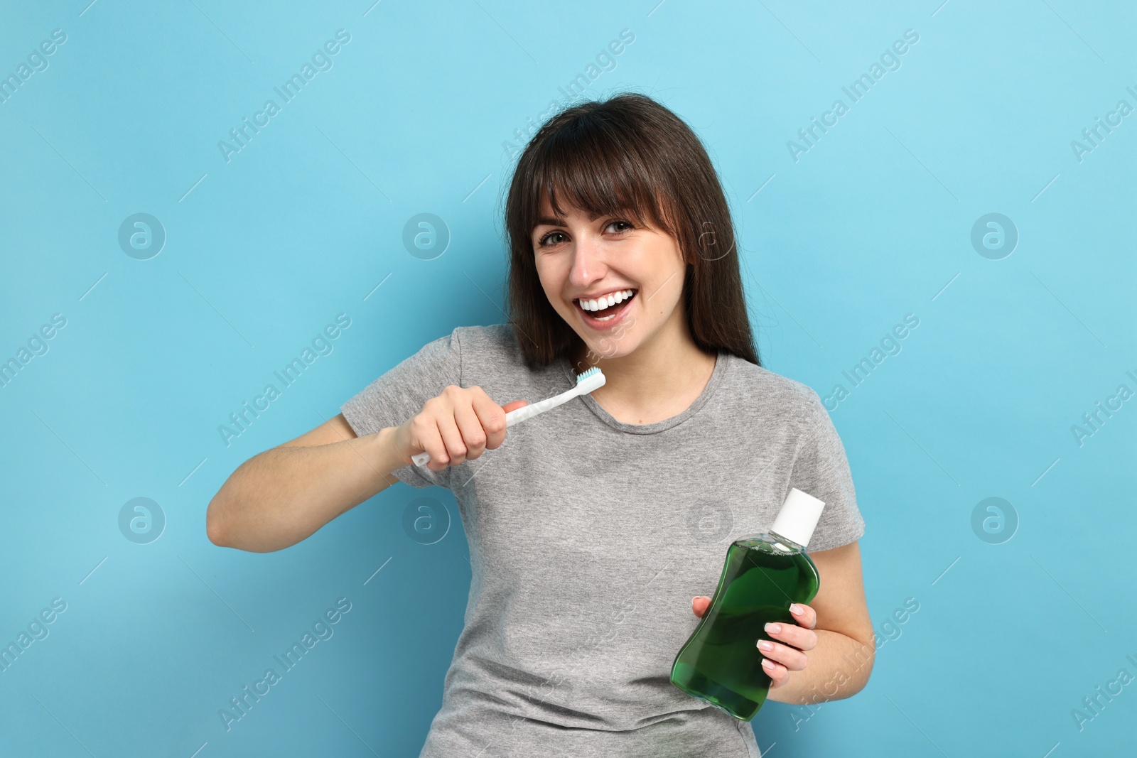 Photo of Young woman with mouthwash and toothbrush on light blue background