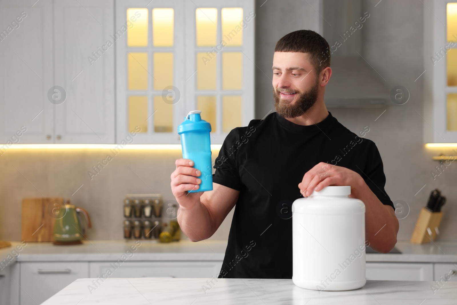 Photo of Young man with shaker of protein and powder at white marble table in kitchen