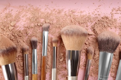 Photo of Makeup brushes and scattered face powder on pink background, flat  lay