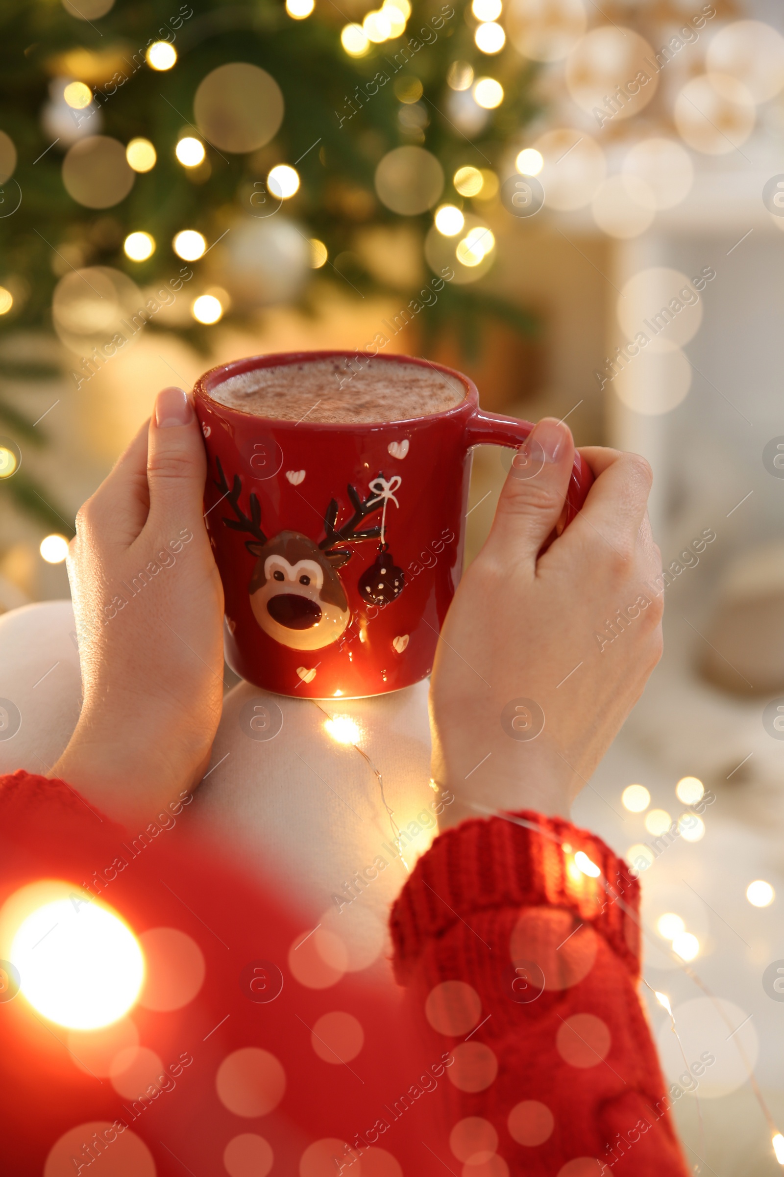 Photo of Woman holding festive cup with coffee near Christmas tree indoors, closeup