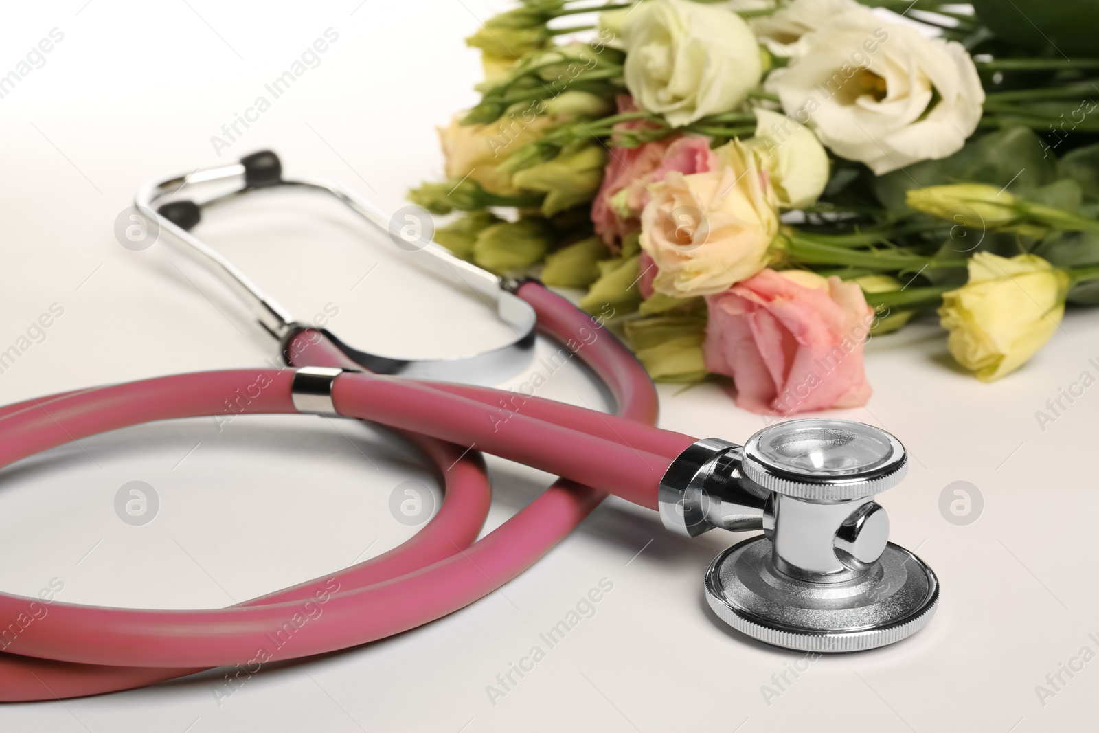 Photo of Stethoscope and eustoma flowers on white background, closeup. Happy Doctor's Day