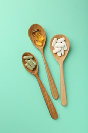 Photo of Different vitamin capsules in spoons on turquoise background, flat lay