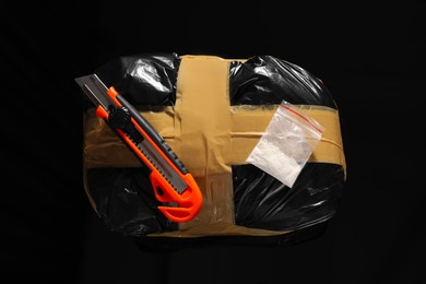 Smuggling, drug trafficking. Packages with narcotics and utility knife on black surface, top view