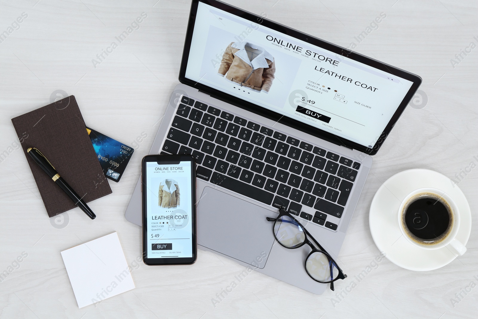 Photo of Online store website on laptop screen. Computer, smartphone, stationery, glasses and coffee on light grey wooden table, flat lay