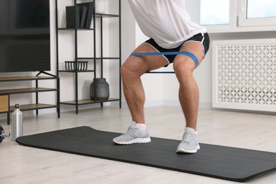 Photo of Athletic man doing exercise with elastic resistance band on mat at home, closeup