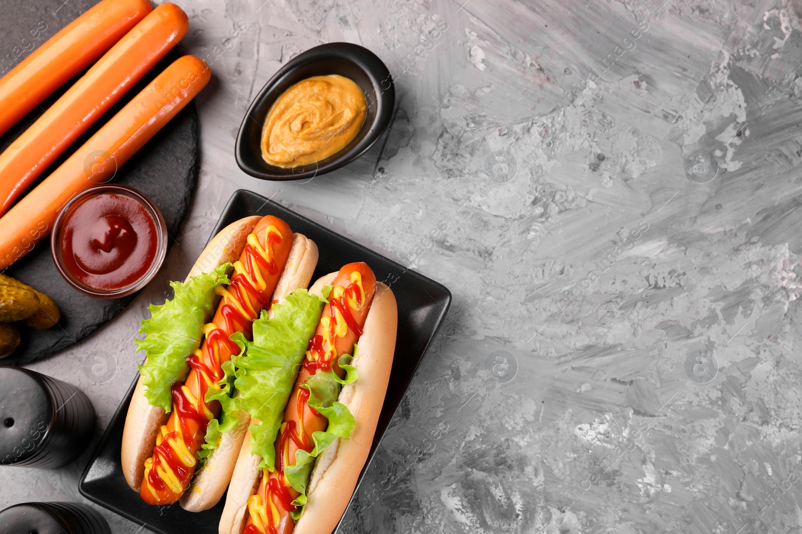 Photo of Tasty hot dogs and ingredients on grey textured table, flat lay. Space for text