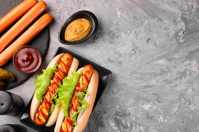 Tasty hot dogs and ingredients on grey textured table, flat lay. Space for text