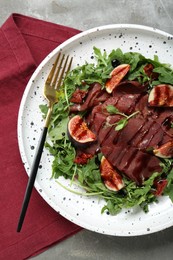 Plate of tasty bresaola salad with figs, sun-dried tomatoes, balsamic vinegar and fork on grey table, top view