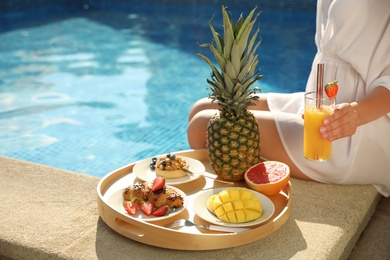 Young woman with delicious breakfast on tray near swimming pool, closeup