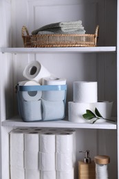 Photo of Toilet paper rolls, green leaves, towels and cotton pads on white shelves