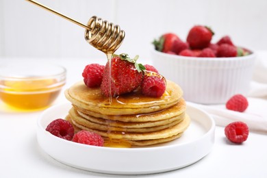 Pouring honey onto tasty pancakes with fresh berries on white table