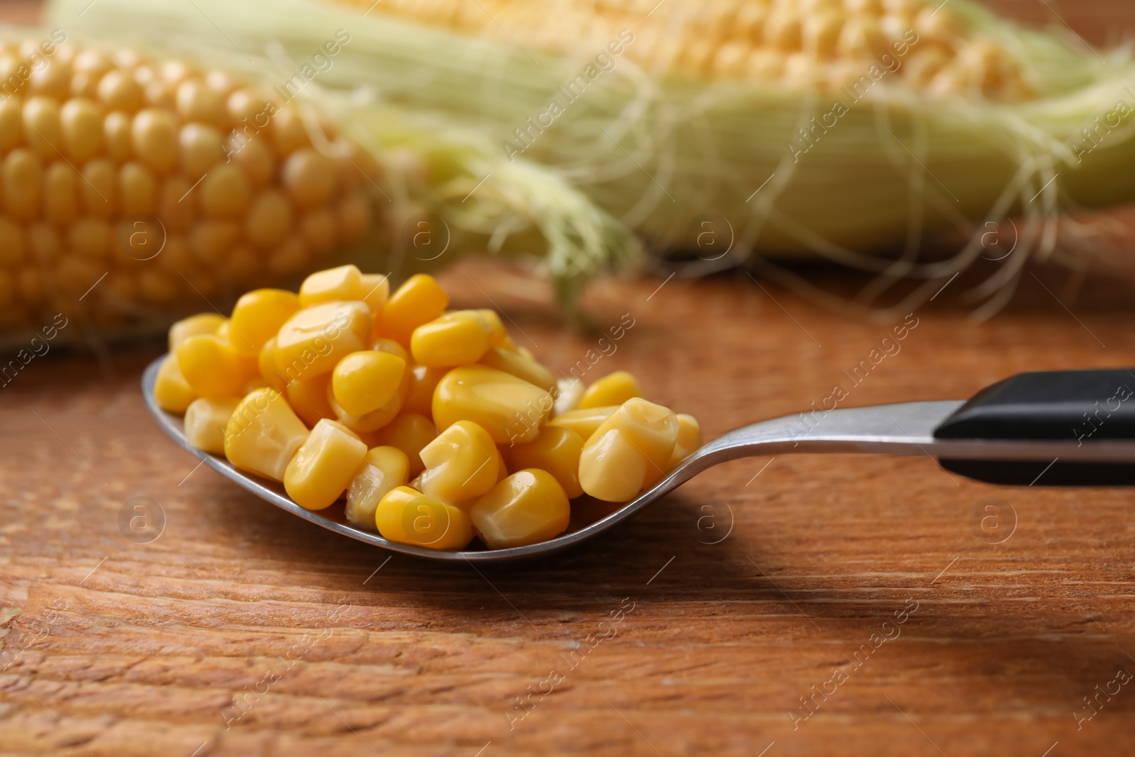 Photo of Spoon of preserved corn on wooden table, closeup