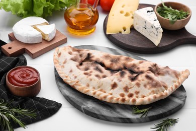 Photo of Tasty pizza calzone with tomato sauce and different products on white table
