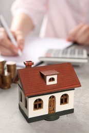 Photo of Woman planning budget at grey table, focus on house model