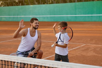 Photo of Little boy giving high five to his father on tennis court