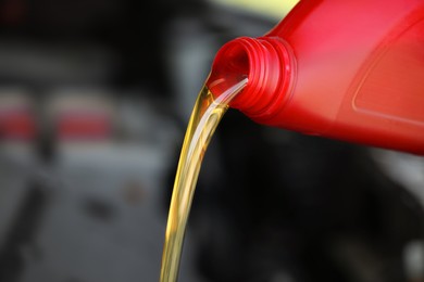 Photo of Pouring motor oil from red container against blurred background, closeup