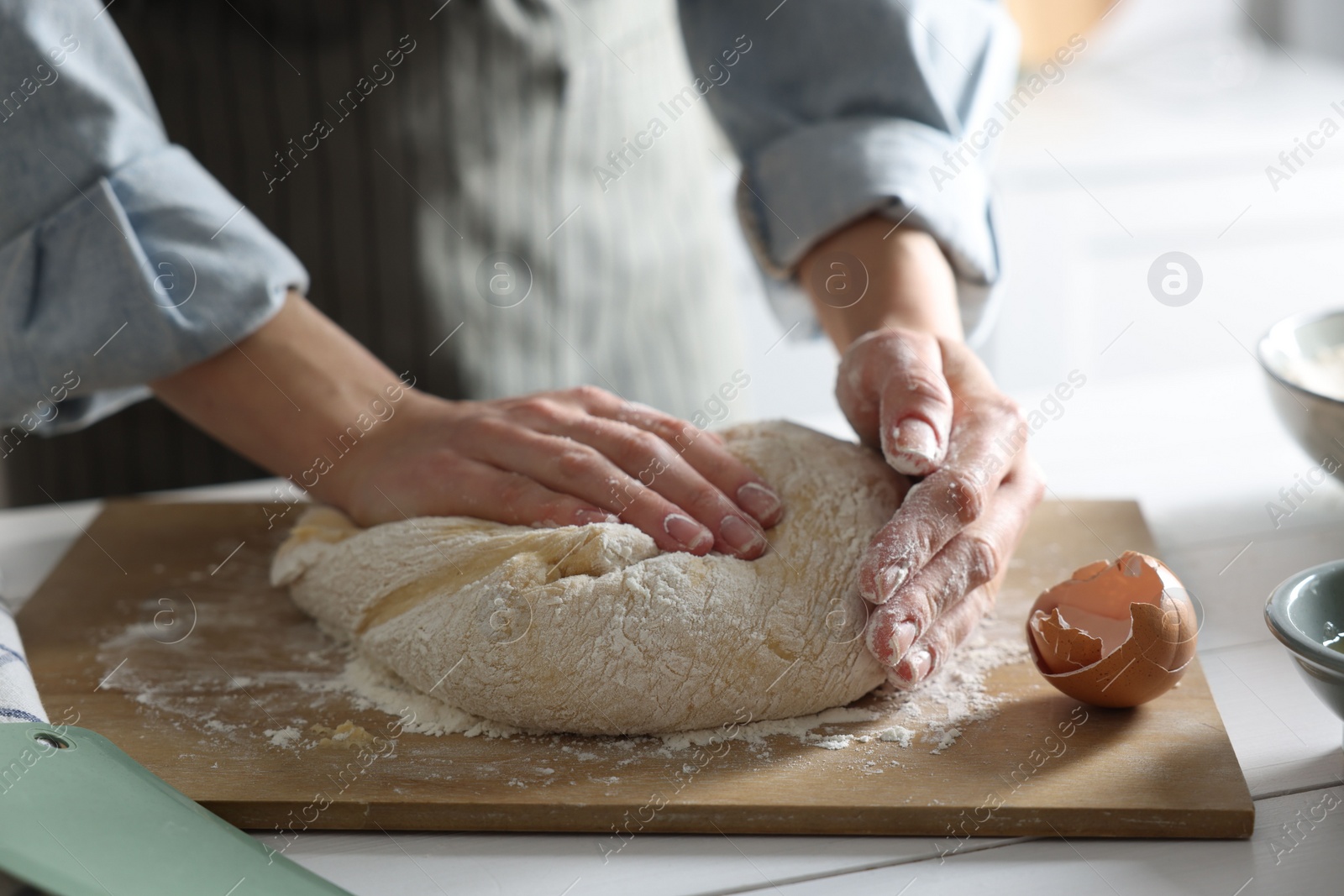 Photo of Woman kneading dough at white wooden table in kitchen, closeup