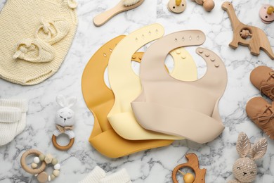 Flat lay composition with silicone baby bibs, toys and accessories on white marble background