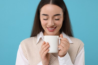 Happy young woman holding white ceramic mug on light blue background