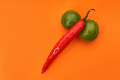 Photo of Chili pepper and limes symbolizing male sexual organ on orange background, flat lay. Potency problem