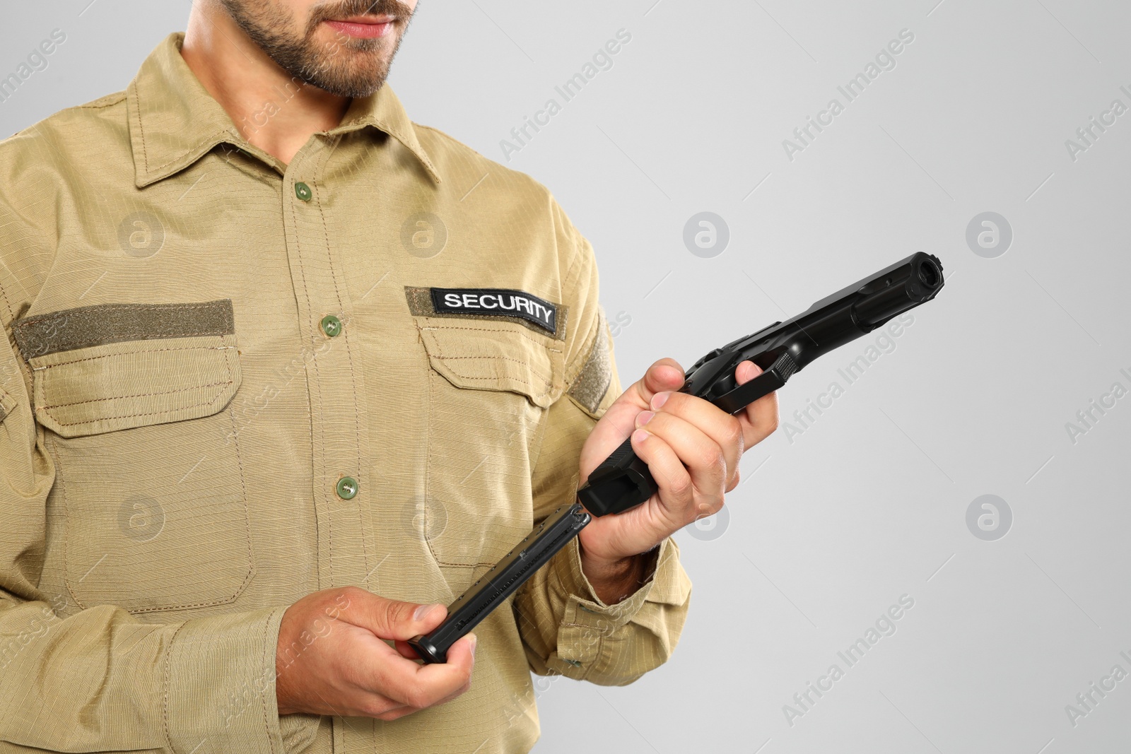 Photo of Male security guard in uniform with gun on grey background, closeup