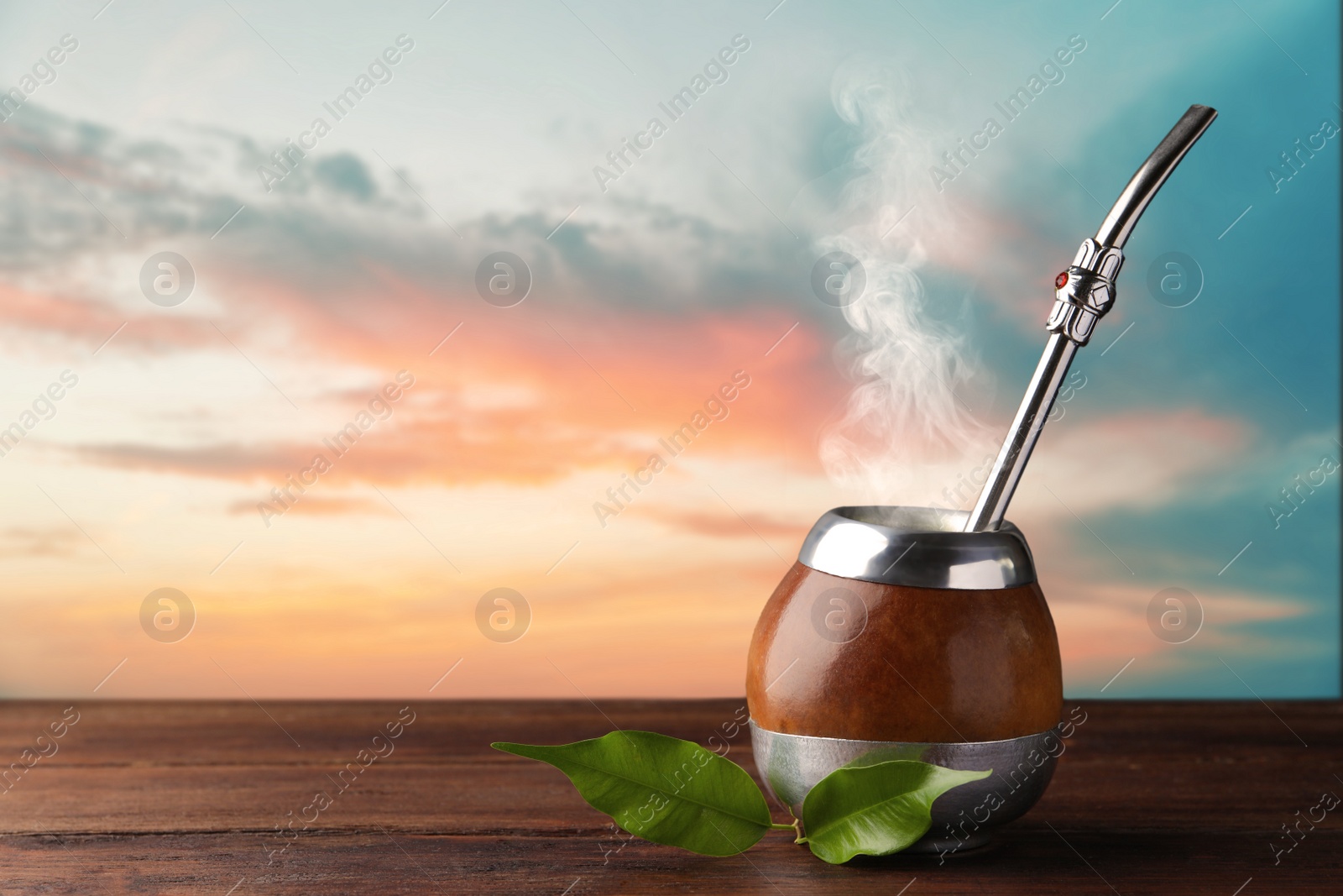 Image of Calabash with mate tea and bombilla on wooden table outdoors at sunset. Space for text