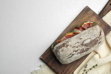 Photo of Delicious sandwich with fresh vegetables and prosciutto on light table, top view. Space for text