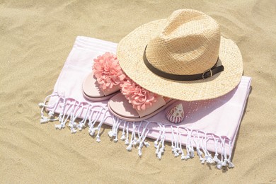 Photo of Blanket with slippers, straw hat and seashell on sand outdoors. Beach accessories