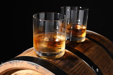 Photo of Glasses of tasty whiskey on wooden barrel, closeup