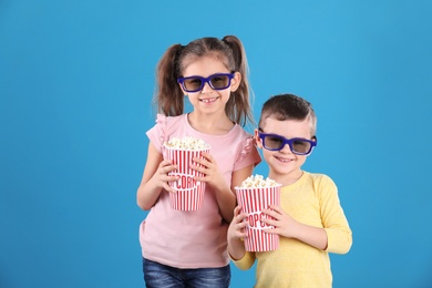 Cute children with popcorn and glasses on color background