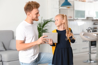 Photo of Happy father giving textbook to little child with school bag at home