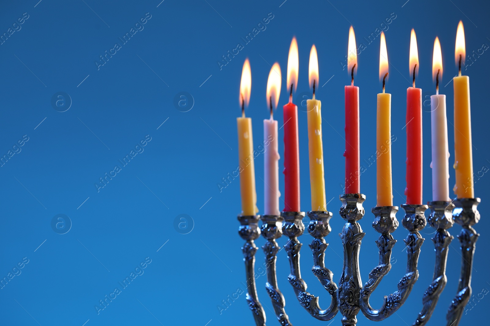 Photo of Hanukkah celebration. Menorah with burning candles on blue background, space for text