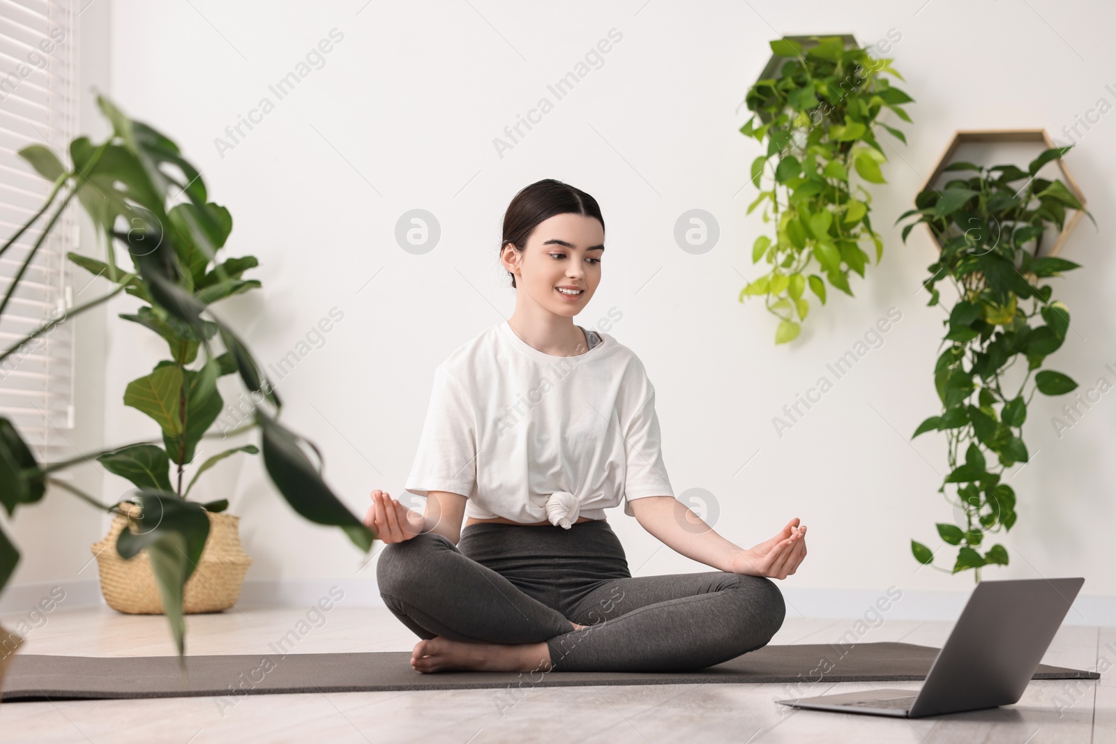 Photo of Beautiful girl meditating on mat near laptop in yoga studio