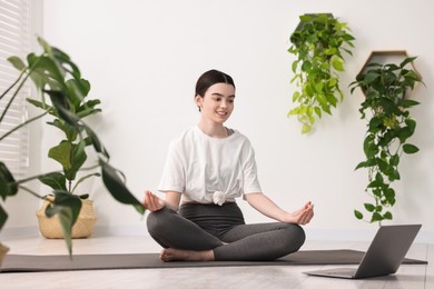 Beautiful girl meditating on mat near laptop in yoga studio