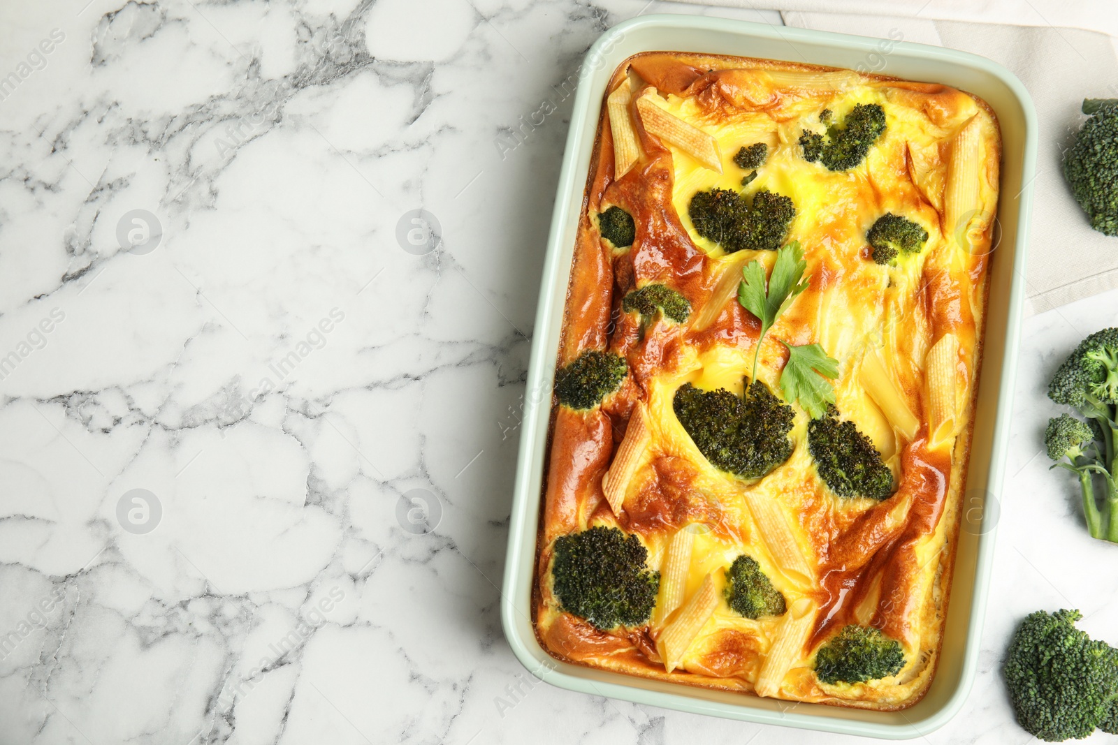 Photo of Tasty broccoli casserole in baking dish on white marble table, flat lay. Space for text