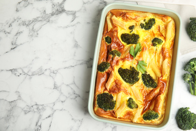 Photo of Tasty broccoli casserole in baking dish on white marble table, flat lay. Space for text