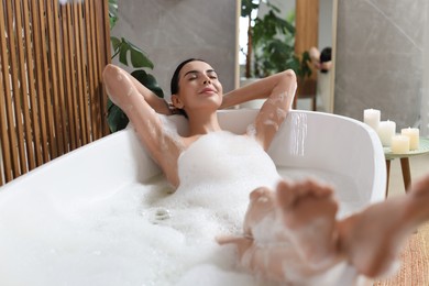 Beautiful young woman taking bubble bath at home