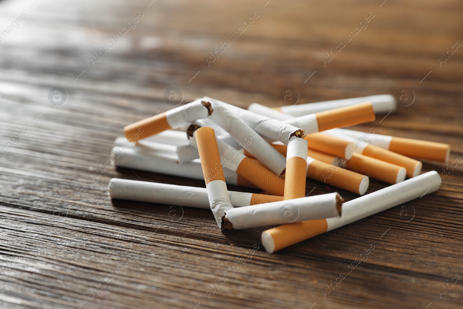 Photo of Stop smoking. Pile of whole and broken cigarettes on wooden table, closeup